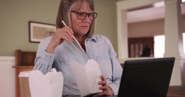 退休的老年妇女在家里吃午饭和使用笔记本电脑 白人女士一边吃东西一边在手提电脑上看东西 — 图库视频影像