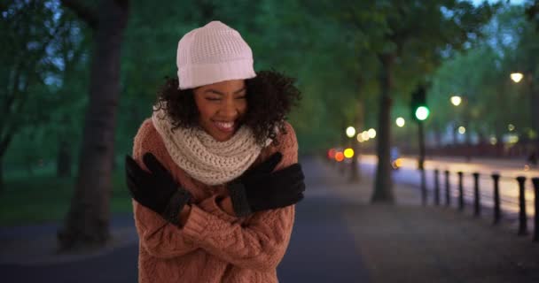 非洲裔美国妇女在等待出租车或骑车人在夜间接她时尽量保暖 在寒冷的冬夜 快乐的黑人女人在街上笑着说寒冷的天气 — 图库视频影像