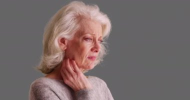 Depresyondaki yaşlı kadının elini gri arka planda boynuna dayadığı yakın plan. Mutsuz, beyaz, üzgün, düşünceli, gri arka planda iç çeken bir kadın. 4k