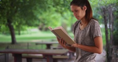 Parkta kitap okuyan güzel bir genç kadın. Mutlu esmer kadın dışarıda eski kitapla rahatlıyor. 4k