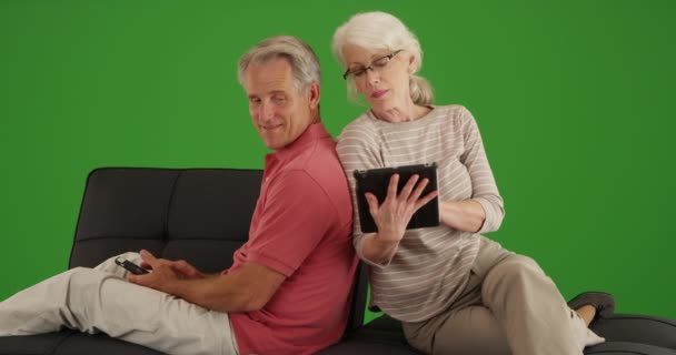 緑色の画面で自宅のソファの上のデバイスを使用してシニアカップル 緑の画面でキーまたは構成されます — ストック動画