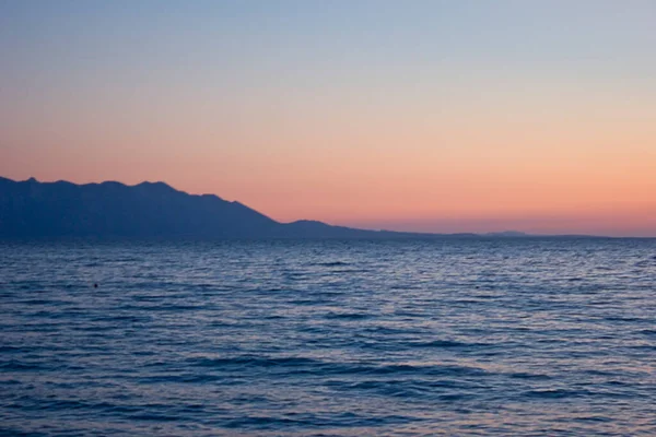 地平線にピンクの夕焼けと青い山々が広がる海 — ストック写真