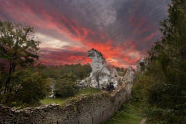 Bir kaya ve taş duvarlı bir manzara. Uçurumun üzerinde parlak kırmızı bir günbatımı