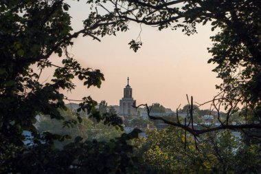 Şehir peyzajı kilisesi, ağaç dallarıyla çerçevelenmiş batan güneşin ışınları altında.
