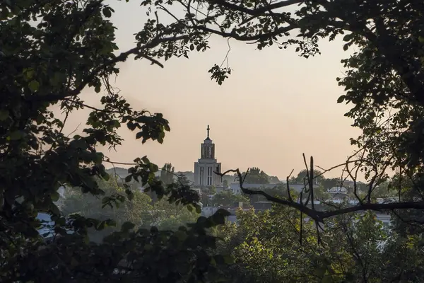 Şehir peyzajı kilisesi, ağaç dallarıyla çerçevelenmiş batan güneşin ışınları altında.