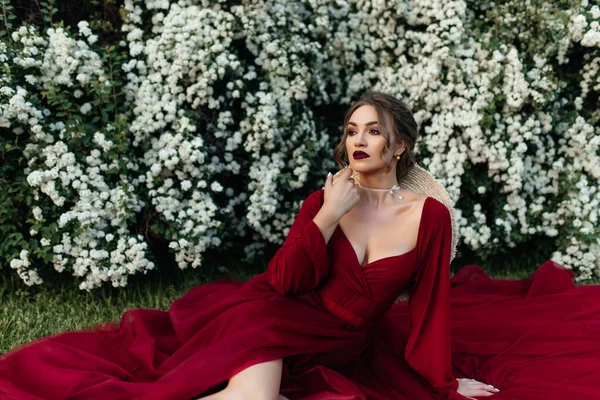 stock image beautiful girl in a red dress sits near a bush with white flowers