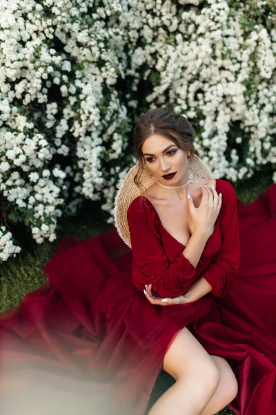 Menina Bonita Vestido Vermelho Senta Perto Arbusto Com Flores Brancas — Fotografia de Stock