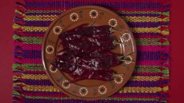 Kırmızı arkaplanda kırmızı bir tabağı kaldıran kuru biberler, masa örtüsü, Pasilla ve Guajillo Meksika baharatı düzlükleri