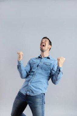 Super happy young bearded Caucasian man in casual jeans shirt looking up and making winners gesture, full length, studio shot, isolated, Copy Space, Vertical