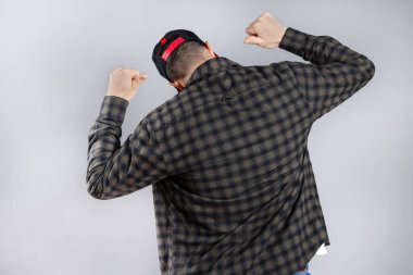Young man standing backwards in casual clothes posing isolated on gray background, studio portrait. Man showing and pointing on his back. Horizontal
