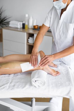 Masadaki kadın, üniformalı güzellik uzmanına ve masadaki saç çıkarma işlemi sırasında ağda bandıyla steril maske takan kadına karşı. Dikey