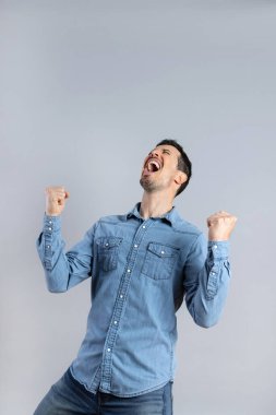 Süper mutlu, sakallı, sıradan kot gömlekli beyaz adam kapalı gözlerle yukarı bakıyor ve kazananlara jest yapıyor, tam boy, stüdyo çekimi, izole edilmiş, kopyalama alanı, dikey