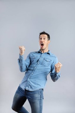 Şaşırmış, sakallı, sıradan kot gömlekli beyaz adam kazanan jest yapıyor, uzun, stüdyo çekimi, izole edilmiş gri arka plan, Kopya Boşluğu, Dikey
