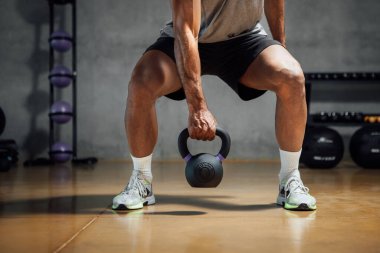 Cropped fit Athletic man lifting weight with kettle bell or dumbbell in gym. Horizontal copy space.