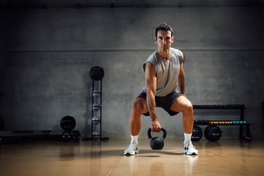 Fit caucasian Athletic man lifting weight with kettle bell or dumbbell with one hand arm in gym. Horizontal copy space, full length