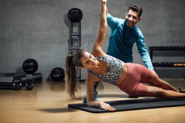 Smiling personal trainer showing right position to do plank exercise during fitness workout in health club. Fitness and gym concept. Horizontal copy space