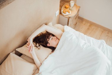 From above Young woman sleeping peacefully on cozy bed in morning, lying down, stretching arms. Top angle copy space, horizontal