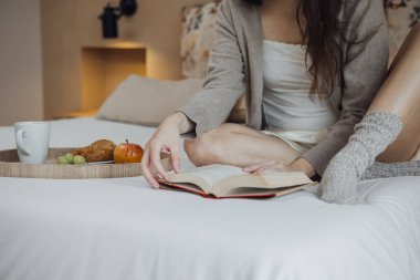 Cropped Anonymous woman reading book on soft bed, front view, copy space, horizontal.