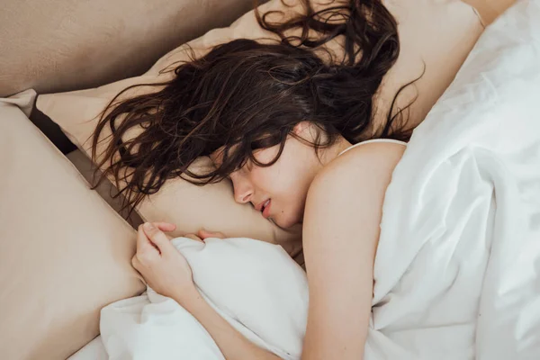 Close up of young brunette woman with long hear sleeping peacefully on cozy bed in morning. Horizontal