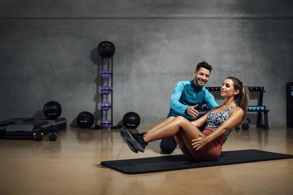 Smiling fitness trainer showing right position to do abs in a gym hiit class. Fitness and gym concept. Horizontal copy space