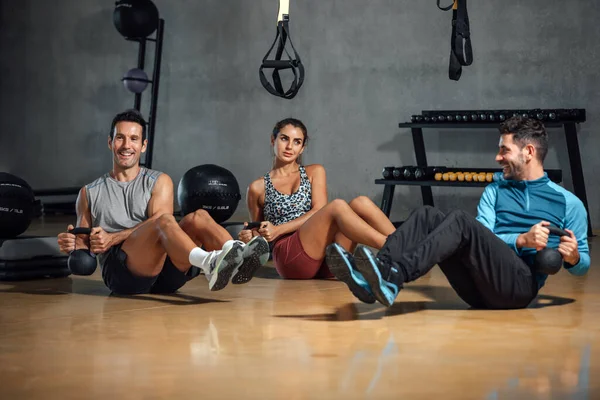 Group of sporty woman and men doing russian twists abs exercises sit up, raising legs and holding kettlebell in gym. Personal trainer showing correct pose for good workout. Horizontal