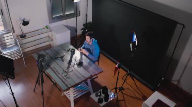 Youtuber or influencer creating video content for social network in a photography studio, reviewing video products. Behind the scenes, 4k video, horizontal, high wide angle shot.