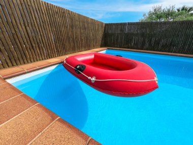 Evin arka bahçesindeki özel bir yüzme havuzunda yüzen kırmızı şişme bot. Yaz, tatil, tatiller, tatil konsepti. İnsan yok. Yatay