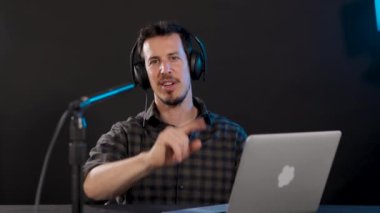 Kamerada, dizüstü bilgisayarı ve kulaklığı olan beyaz bir adamın kameraya bakıp sosyal medya izleyicileriyle konuştuğu görülüyor. Yatay, 4k video.