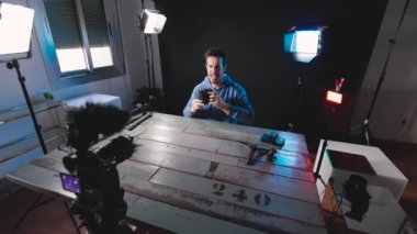 Kameraya yeni video ekipman ve cihazları göstererek, bir fotoğraf stüdyosunda sosyal ağ için video içeriği oluşturan erkek Youtuber veya nüfuz edici. Yapım, 4k video, yatay, geniş açı çekim.