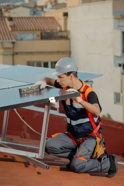Professional worker installing solar energy panels on the roof of a house. Engineer with level tool checking photovoltaic cells. Alternative energy power sustainable resources. Copy space