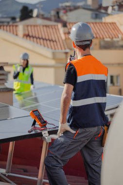 Bir binanın çatısında, güneş paneli kurulumu sırasında telsiz ya da taşınabilir radyo vericisi kullanan teknik mühendis grubu. Dikey ve odaklanmış arkaplan