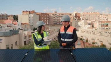 Teknik mühendisler fotovoltaik bir çatıdaki tesisatın gelişimini kontrol ediyorlar. Güneş panelleri bakım ve teftişinde çalışan kadın ve erkek. Ön görünüm, 4k yatay görüntü