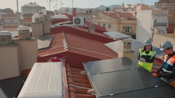 男工程师和女技术员在建筑物屋顶安装太阳能电池板时交谈 空中视图 水平4K视频 跟踪镜头 — 图库视频影像