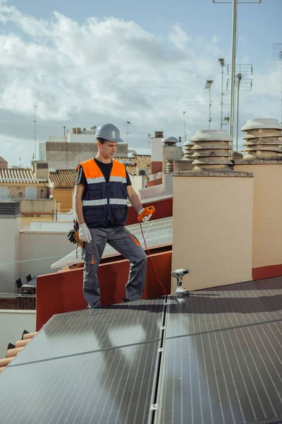 stock image Technical engineer installs photovoltaic energy cells on a city house roof. Worker tests urban household solar panels with multimeter during maintenance revision. Alternative energy. Vertical