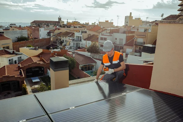 stock image Professional engineer worker installing solar energy panels on a house roof. Technician with electric looking multimeter during maintenance of photovoltaic cells. Wide angle, horizontal