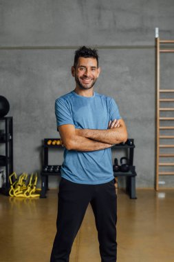 Spor kulübünde kameraya bakan, kendine güvenen, gülümseyen İspanyol adamın portresi. Spor salonunda kollarını kavuşturan beden eğitimi hocası. Gerçek insanlar, iş hayatı kavramı. Dikey