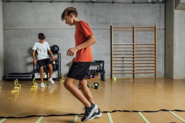 Spor salonunda beton duvarla antrenman yapan bir sürü genç çocuk. Egzersiz, ağırlık kaldırmak, zıplamak. Yatay.