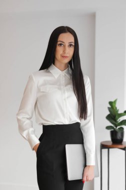 Kurumsal portre kendine güvenen zarif, uzun saçlı beyaz kadın, ofisinde ya da evinde duruyor, dizüstü bilgisayarını tutuyor, kameraya bakıyor. Yönetici, iş kadını. Dikey.