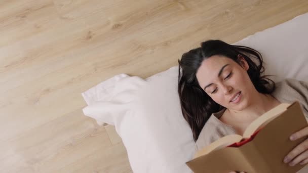 梦中年轻的黑发女人穿着睡衣 躺在床上看书 顶部视图 高角镜头 高质量的4K镜头 — 图库视频影像