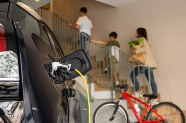 Evde tanınmayan bir aile merdivenleri çıkarken ev elektriği istasyonunda şarj olan elektrikli araç prizini kapatın. Enerji Bilinci, Sürdürülebilir Kaynaklar. Bulanık arkaplan, Yatay