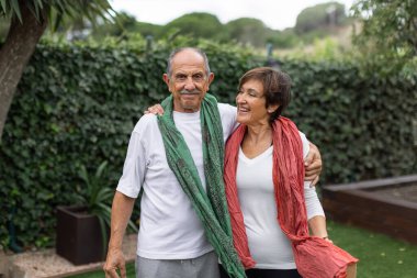 Yaşlı bir çift dışarıda güzel ve sıcak bir anı paylaşıyor. Renkli, rahat eşarplara sarılıp dinlenme tesisinde yoga ve meditasyon yaptıktan sonra gülümsüyor. Yatay.