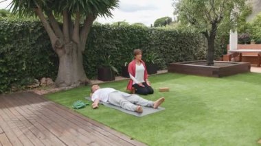 Son sınıf çifti, huzur dolu bir bahçe ortamında meditasyon ve rahatlama sanatını sergileyerek yoga minderleri üzerinde birlikte meditasyon yapıyorlar. İzleme görüntüsü, yatay 4k video