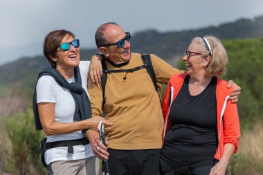 Spor giyim sektöründeki üç neşeli son sınıf öğrencisi doğa yürüyüşü maceralarının tadını çıkarıyorlar. Güneş gözlüğü takıyorlar, birlikte gülüyorlar, dağlarla çevrili yürüyüş direkleri tutuyorlar. Aktif yaşam tarzı ve arkadaşlık.