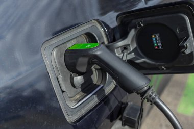 Fişi takılı elektrikli bir aracın şarj portuna yakın çekim. Şarj aletinin yeşil detayları. Teknoloji ve sürdürülebilirliğe odaklan.