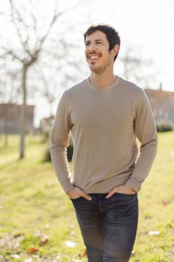 Mutlu gülümseyen orta yaşlı beyaz adam güneşli bir günde dışarı çıkıyor. Onun rahat duruşu ve neşeli ifadesi pozitifliği iletir. Ağaçlar ve binalarla dikey, bulanık arkaplan.