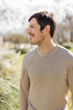 Orta yaşlı, beyaz bir adam sakin bir ifadeyle, doğa ve temiz havanın tadını çıkararak uzaklara bakıyor. Yumuşak güneş ışığı, sakin atmosferi güçlendirir. Dikey, bulanık arkaplan, sıcak ve huzurlu bir ortam..