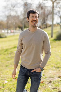 Orta yaşlı bir adam güneşli bir parkta yürüyor, doğal ve rahat bir ifadeyle yan tarafa bakıyor. Onun sakin tavrı stresten arınmış bir davranışı yansıtıyor. Ağaçlar ve çimenler dikey, bulanık arkaplan