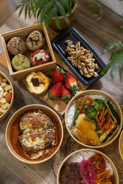 Taze yemek, salata ve ahşap bir masada, çevre dostu kâselerdeki tatlıları tepeden tırnağa görmek. Kurabiye, peynirli kek, sebze, pirinç, et ve taze meyve içerir. Dikey