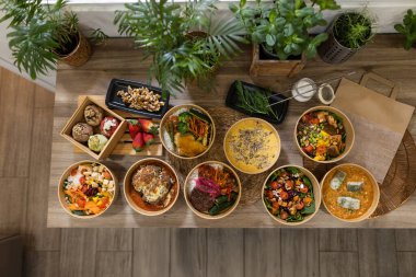 Tahta bir masada, çevre dostu kâselerde servis edilen çeşitli sağlıklı yemekleri tepeden tırnağa görmek. Taze salatalar, çorbalar, pirinç tabakları ve doğal malzemeler ve bitkilerle çevrili tatlılar.