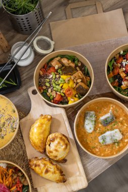 Renkli kinoa kaseleri, zengin çorbalar ve altın-kahverengi böreklerin yer aldığı gurme paket servis yemekleri. Modern yemeklerde taze, besleyici, ve görsel olarak çekici, sürdürülebilirlik. Yukarıdan aşağıya görünüm